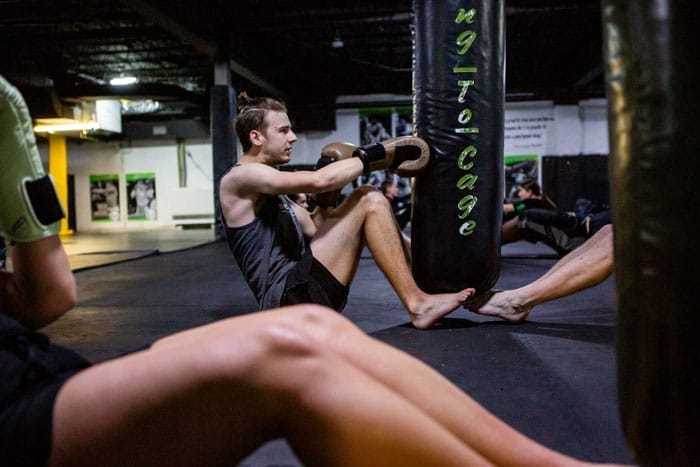 Man performing sit-ups while holding a kettlebell during MMA conditioning training at a martial arts gym