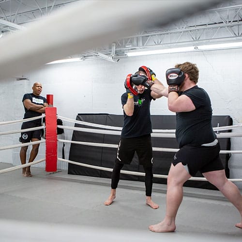 Coach watching two guys on boxing training in the ring